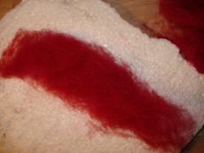 Die rote Alpenwolle als schmales Band auslegen, im Beispiel ist es etwa 3 cm breit und 20 cm lang...